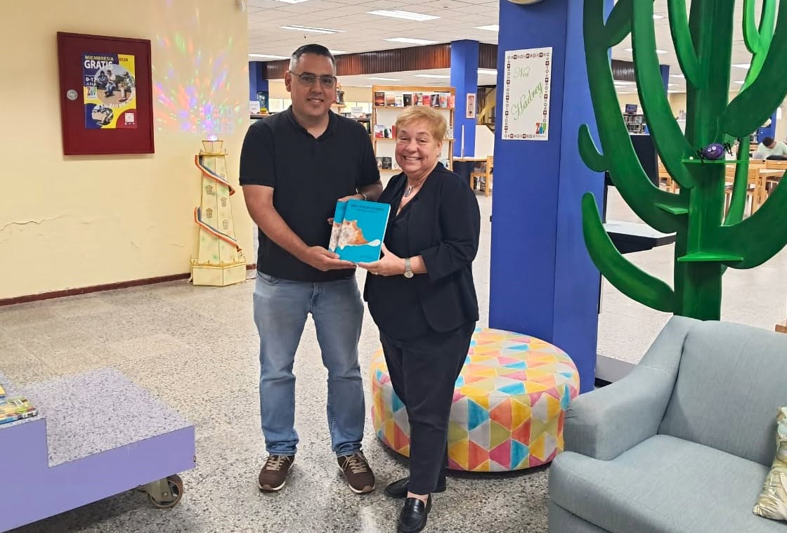 Rendell de Kort handing two copies of The Conch Paradox to Astrid Britten, director of Biblioteca Nacional Aruba